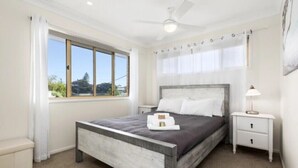 A bedroom with a bed, a nightstand, a ceiling fan, a window, and a view of the outdoors.