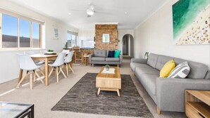 A modern living room with a dining area, grey sofas, and a brick accent wall.