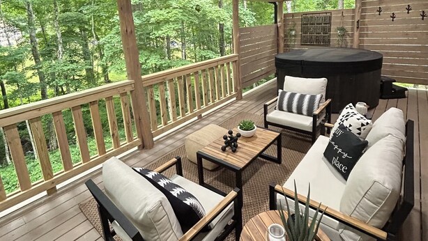 A covered outdoor seating area with wooden furniture, a coffee table, and a view of a forest.
