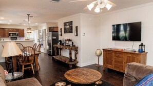 Un salon spacieux avec une table basse ronde en bois, un canapé et un téléviseur fixé au mur.