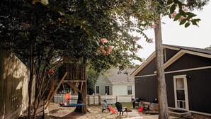Un jardin avec une structure de jeux en bois, une balançoire et un espace détente avec des chaises.
