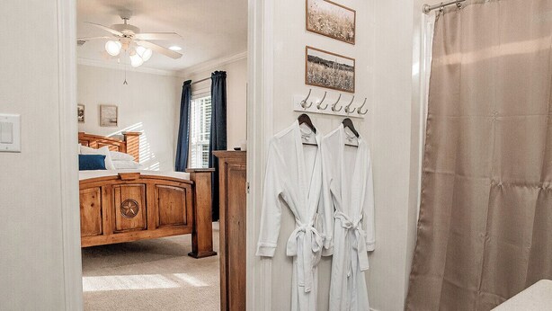 Une chambre à coucher avec un lit en bois, un ventilateur de plafond et une salle de bain avec un rideau de douche.
