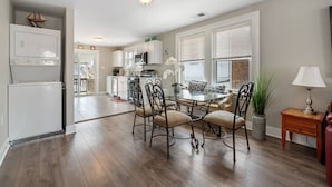 A modern kitchen with white cabinets, a dining area with a glass table and metal chairs, and a small side table with a lamp. - 3BR Bayside Retreat - Beach Gear Included (Ventnor City)