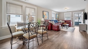 A spacious living room with a red sectional sofa, a glass coffee table, and a dining area with a glass table and metal chairs. - 3BR Bayside Retreat - Beach Gear Included (Ventnor City)