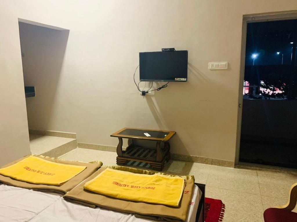 A hotel room with a bed, a small table, a television, and a view of the outside at night.