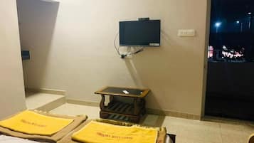 A hotel room with a bed, a small table, a television, and a view of the outside at night.
