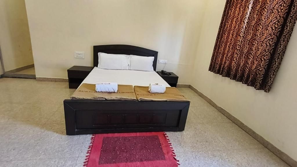 Habitación de hotel con una cama individual, una mesita de noche, un tapete rojo y una cortina estampada.