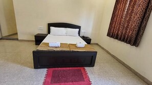 Une chambre d’hôtel avec un lit simple, une table de chevet, un tapis rouge et un rideau à motifs.