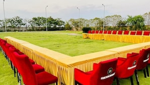 A long conference table with red chairs, set up outdoors on a grassy field. - The Aurum Zurich Club Kalaburgi (Gulbarga)
