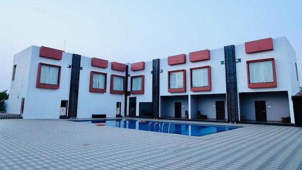 A modern hotel with a pool area, featuring a symmetrical facade with red accents and large windows. - The Aurum Zurich Club Kalaburgi (Gulbarga)