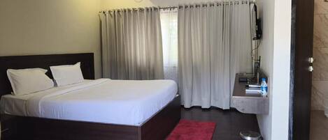 A hotel room with a large bed, a bedside table with a lamp, a small sink, and a red rug.