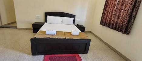 A hotel room with a single bed, a nightstand, a red rug, and a patterned curtain.