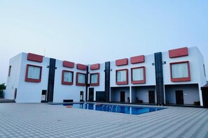 Un hôtel moderne doté d’un espace piscine, avec une façade symétrique agrémentée d’éléments rouges et de grandes fenêtres.