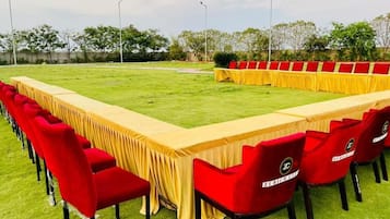Een lange vergader tafel met rode stoelen, buiten op een gazon.