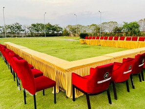 Ein langer Konferenztisch mit roten Stühlen, draußen auf einer grünen Wiese aufgestellt.