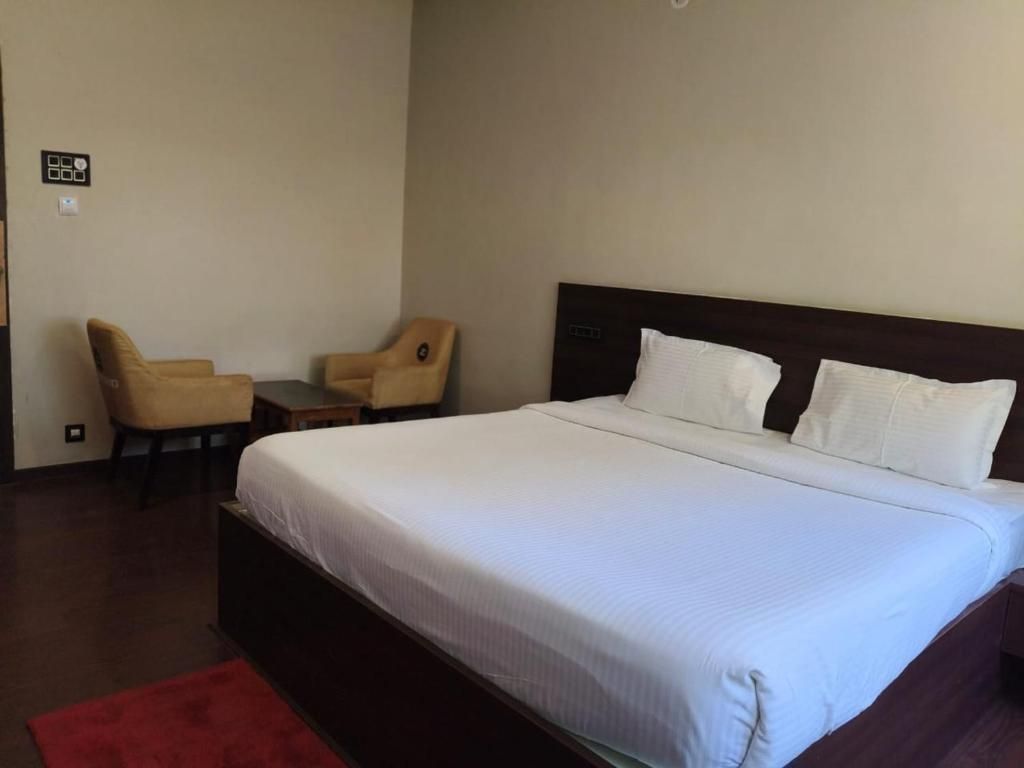 Una camera d'albergo con un letto grande, due poltrone, un tavolino e un tappeto rosso.