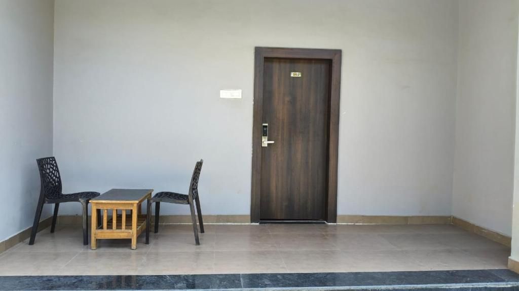 A room with a dark wooden door, a small wooden table, and two black chairs.