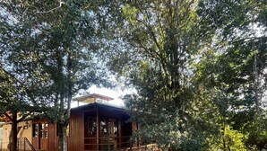 Una cabana rústica amb fonaments de pedra, façana de fusta i un balcó amb vista a un jardí.