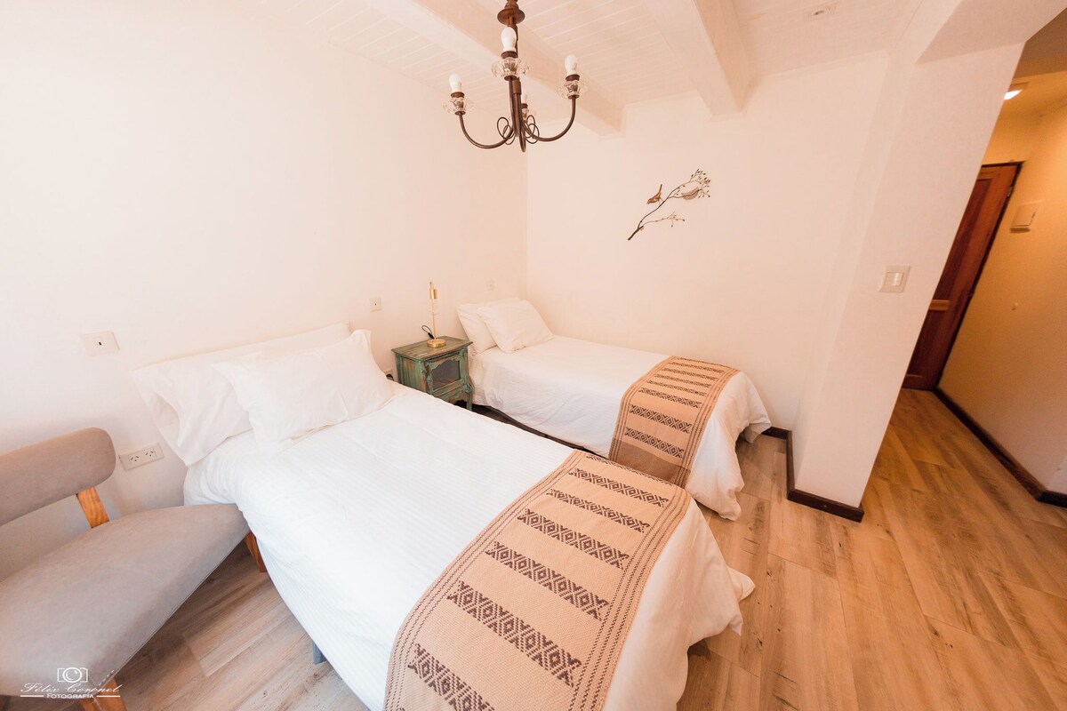 Una stanza con due letti, pavimento in legno, un lampadario e un tavolino con una lampada.
