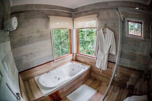 Un baño con bañera, ducha y ventana con vista a follaje.