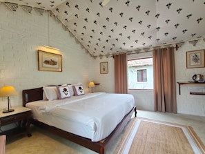 A bedroom with a bed, two bedside tables, a nightstand, a window with curtains, and a wall with framed pictures. - Camp Lands End (Pushkar)