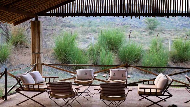 Un espacio exterior con seis sillas y una mesa, rodeado por una valla de bambú, con vistas a un paisaje natural.