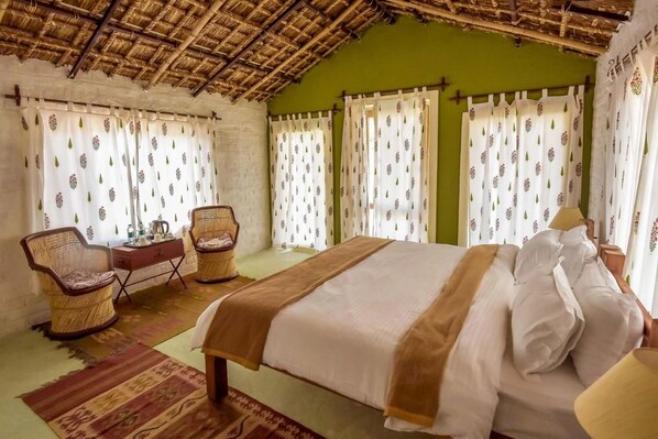 A bedroom with a bed, two wicker chairs, a small table, and a thatched roof ceiling. - Camp Lands End (Pushkar)