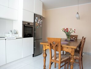 A modern kitchen with white cabinets, a stainless steel refrigerator, and a dining table with chairs. - La Perla (Międzyzdroje)