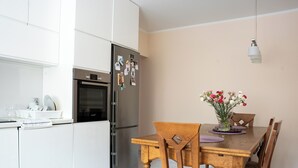 A modern kitchen with white cabinets, a stainless steel refrigerator, and a dining table with chairs. - La Perla (Międzyzdroje)