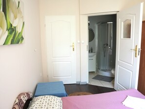 A bedroom with a bed, a bedside table, a door, and a bathroom visible through an open door. - La Perla (Międzyzdroje)