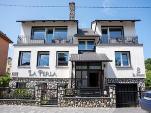 A two-story building with a stone facade, balconies with metal railings, and a sign indicating the name 'LA PERLA'. - La Perla (Międzyzdroje)