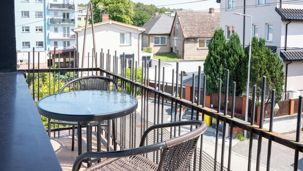 A balcony with a round table and wicker chairs, overlooking a residential area with houses and trees. - La Perla (Międzyzdroje)