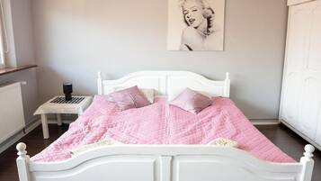 A bedroom with a white bed, pink bedding, a small bedside table, a lamp, and a framed picture on the wall.