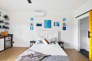 Un dormitorio moderno con cama, mesitas de noche, armario empotrado, zona de cocina con refrigerador y baño con ducha.