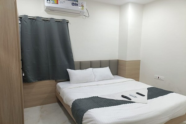 Una camera d'albergo con un letto, una tenda grigia, una testiera bianca, un comodino e un condizionatore d'aria a parete.