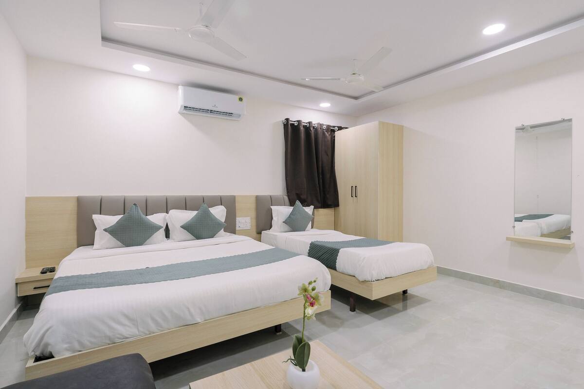 A modern hotel room with two single beds, a wardrobe, a mirror, and an air conditioning unit.