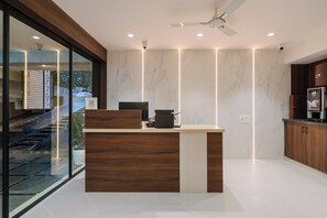 A modern reception desk with a wooden finish, a coffee machine, and a view of a staircase leading outside. - Hotel Saffron Groves (Hyderabad)