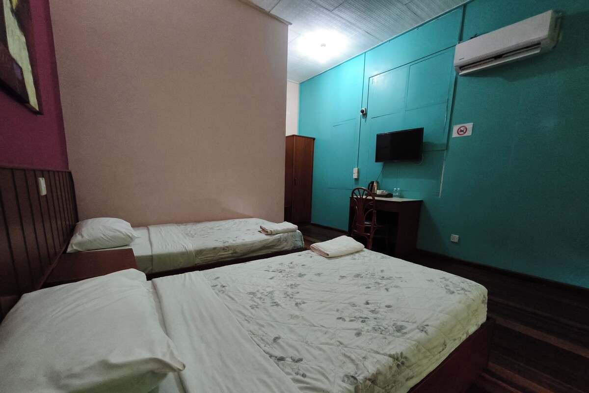 A room with two beds, a desk, a chair, and an air conditioning unit.