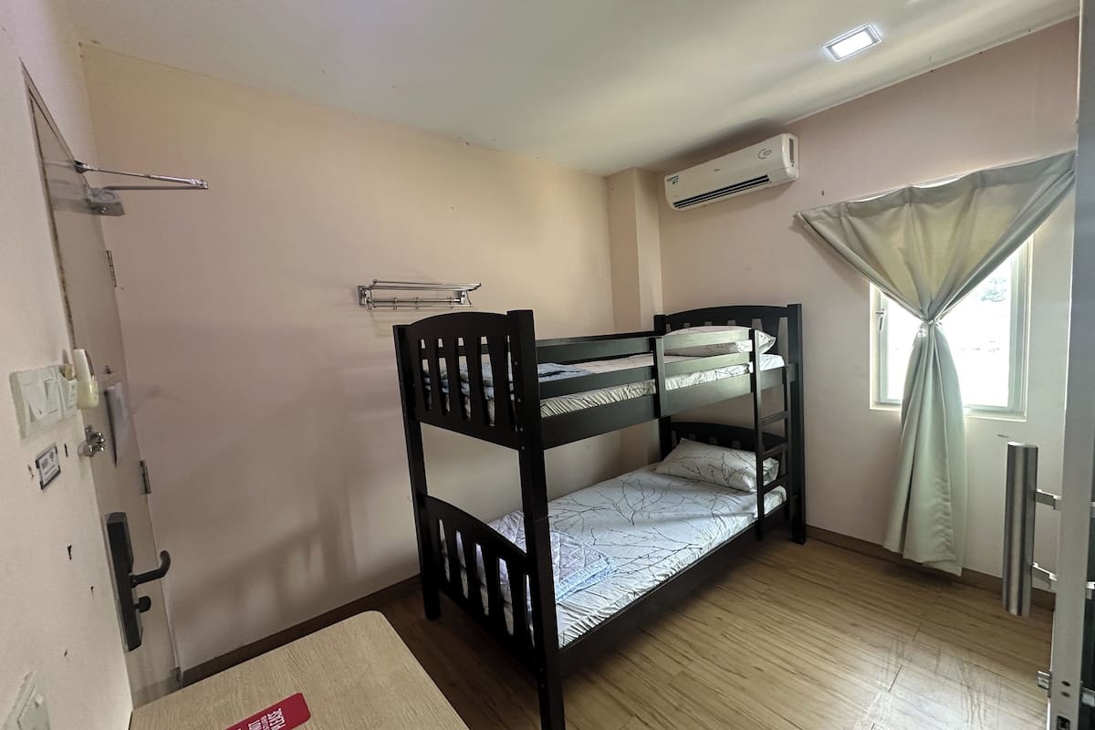 Habitación con literas, piso de madera, ventana con cortinas, aire acondicionado y puerta con manija.