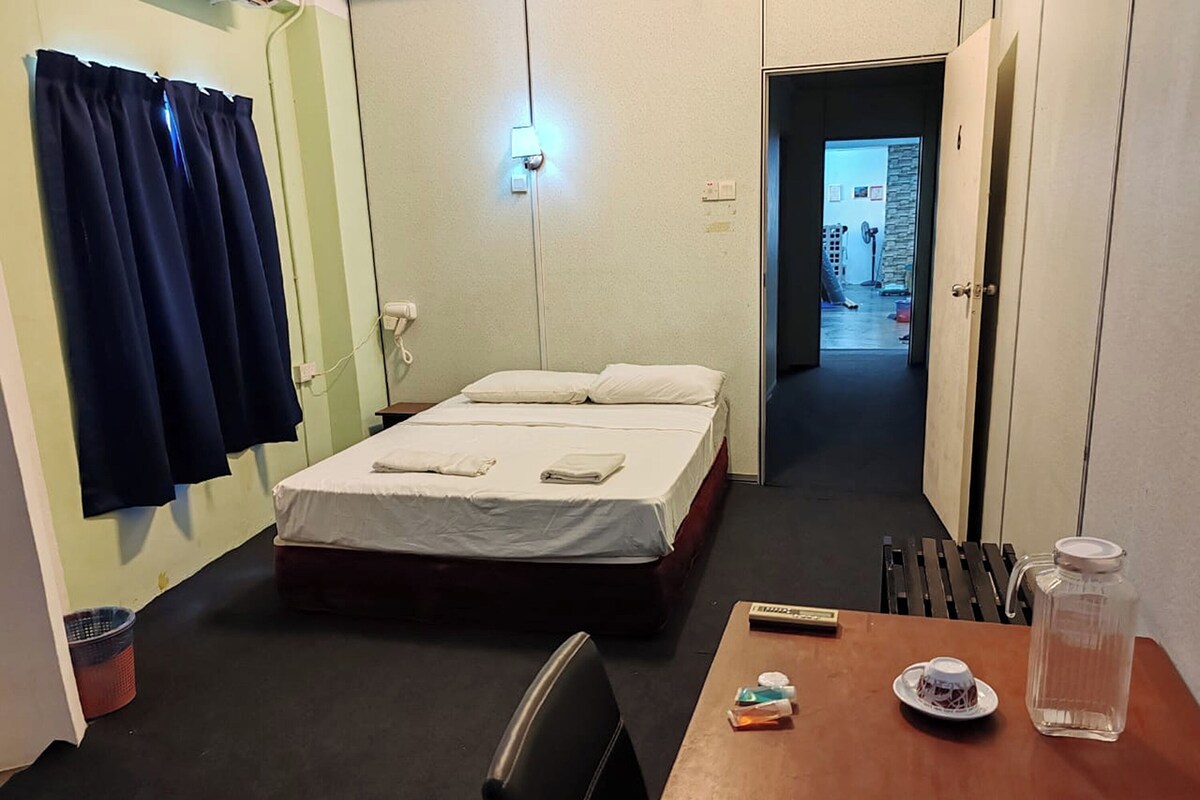 Ein Hotelzimmer mit einem Bett, einem Tisch mit Fernbedienung, einem Glasbehälter und einer Flasche.