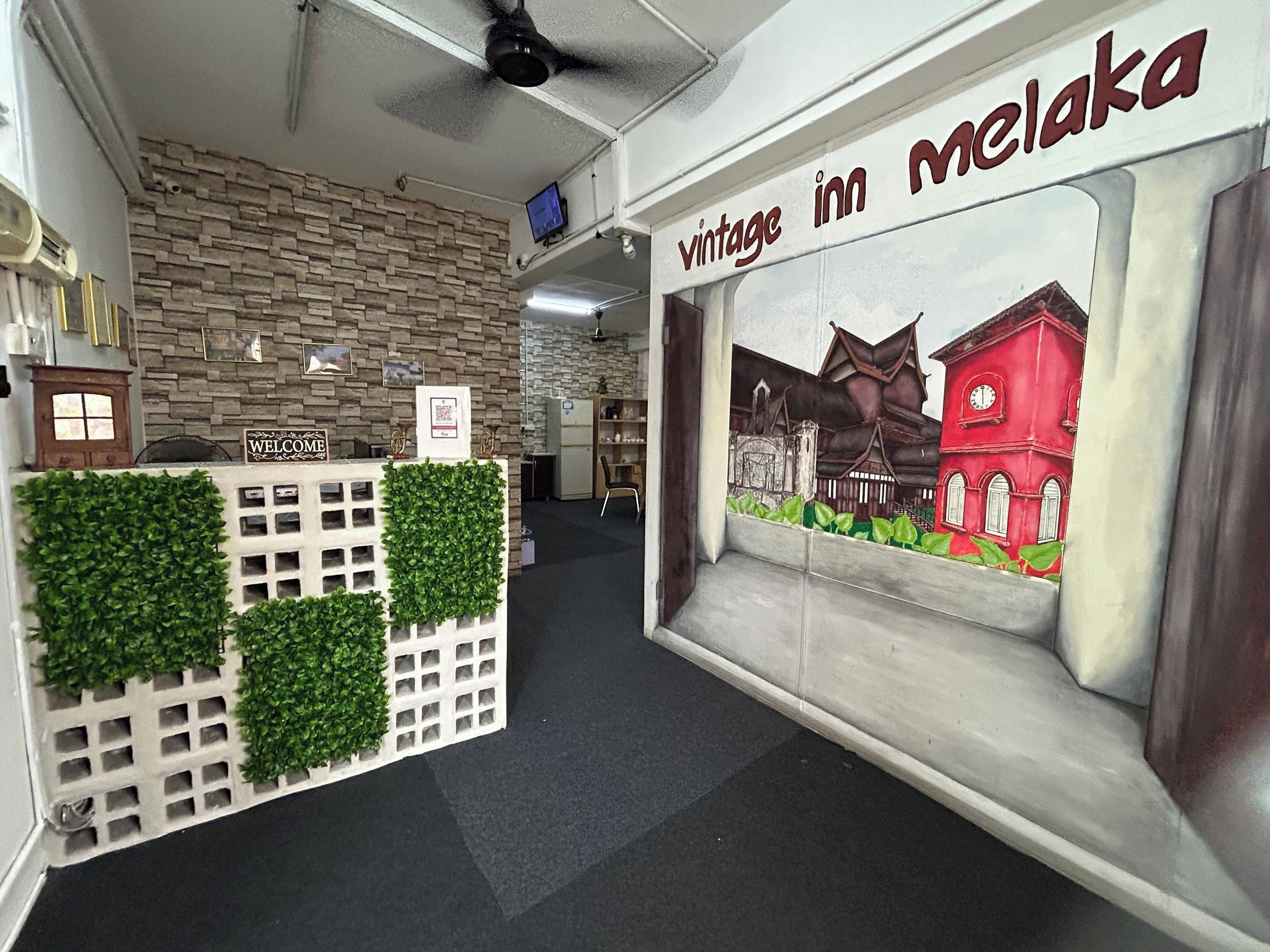A reception area with a brick wall, a welcome sign, a reception desk, and a wall mural depicting a red building.