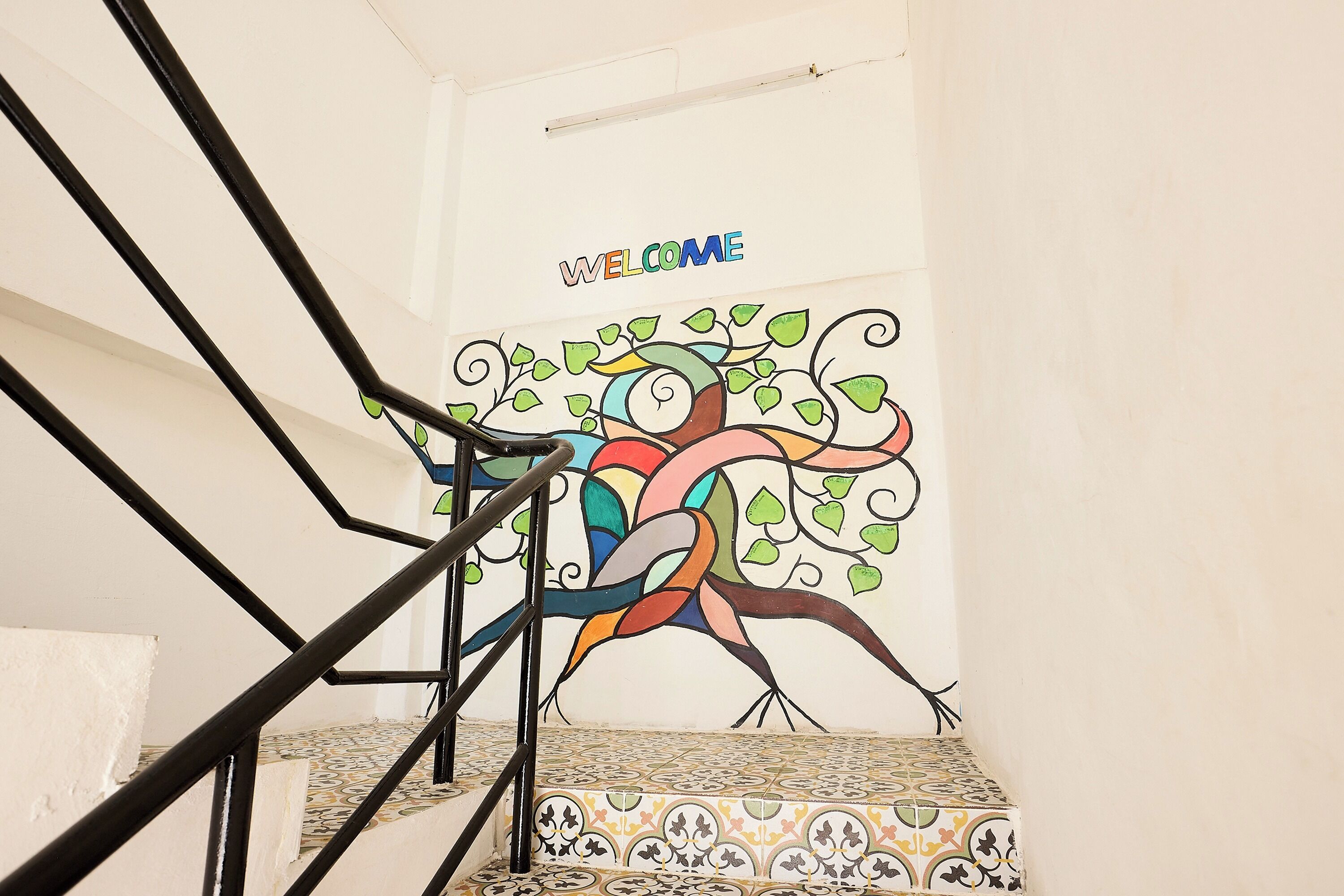 A staircase with a 'WELCOME' sign, a colorful mural, and patterned floor tiles.