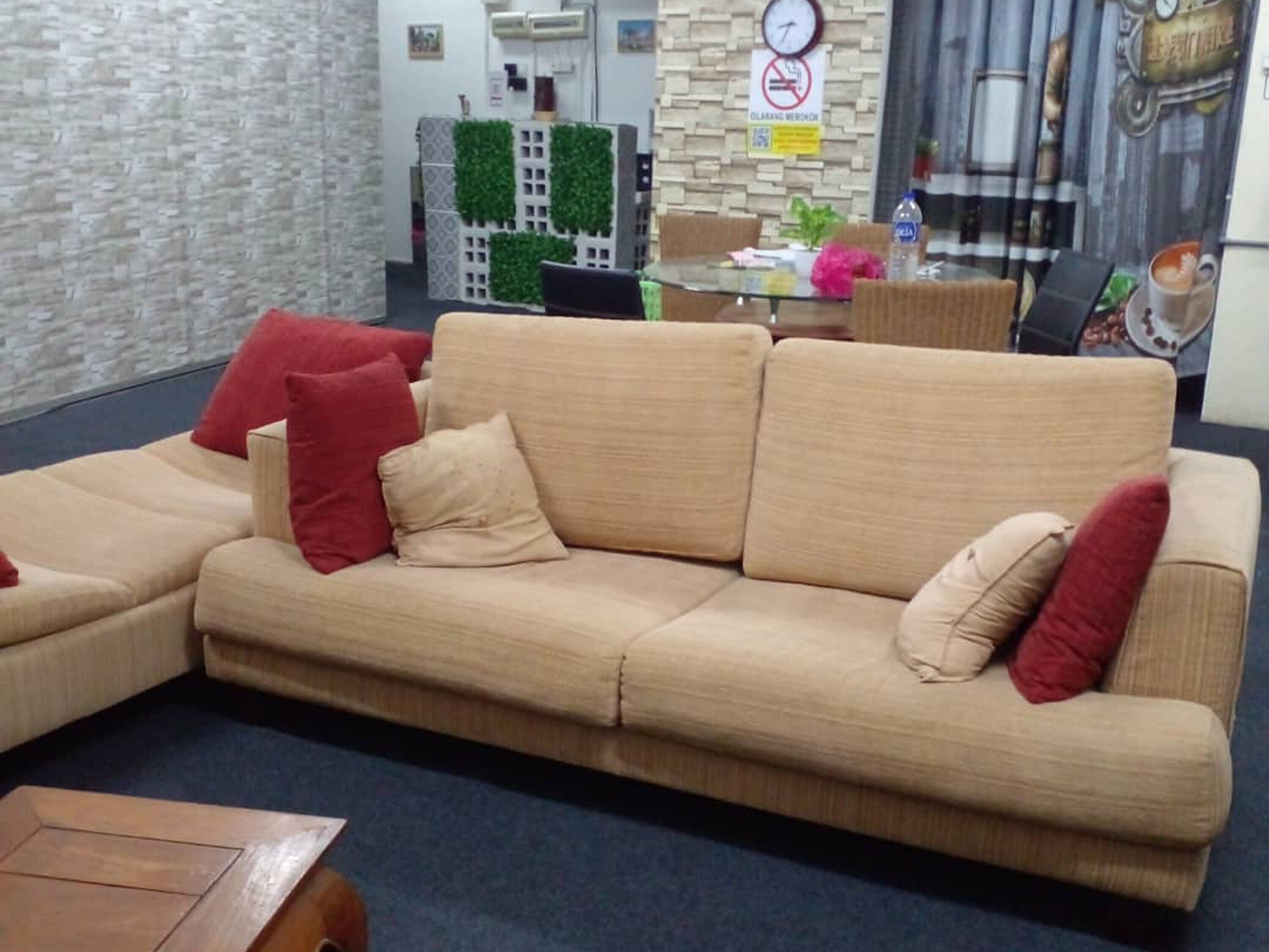 A beige sectional sofa with red and beige cushions in a room with a stone wall and a clock.