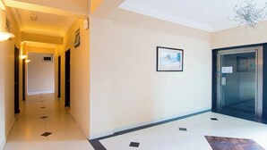 Un hall d’hôtel avec un sol carrelé, un tableau encadré au mur et un ascenseur.
