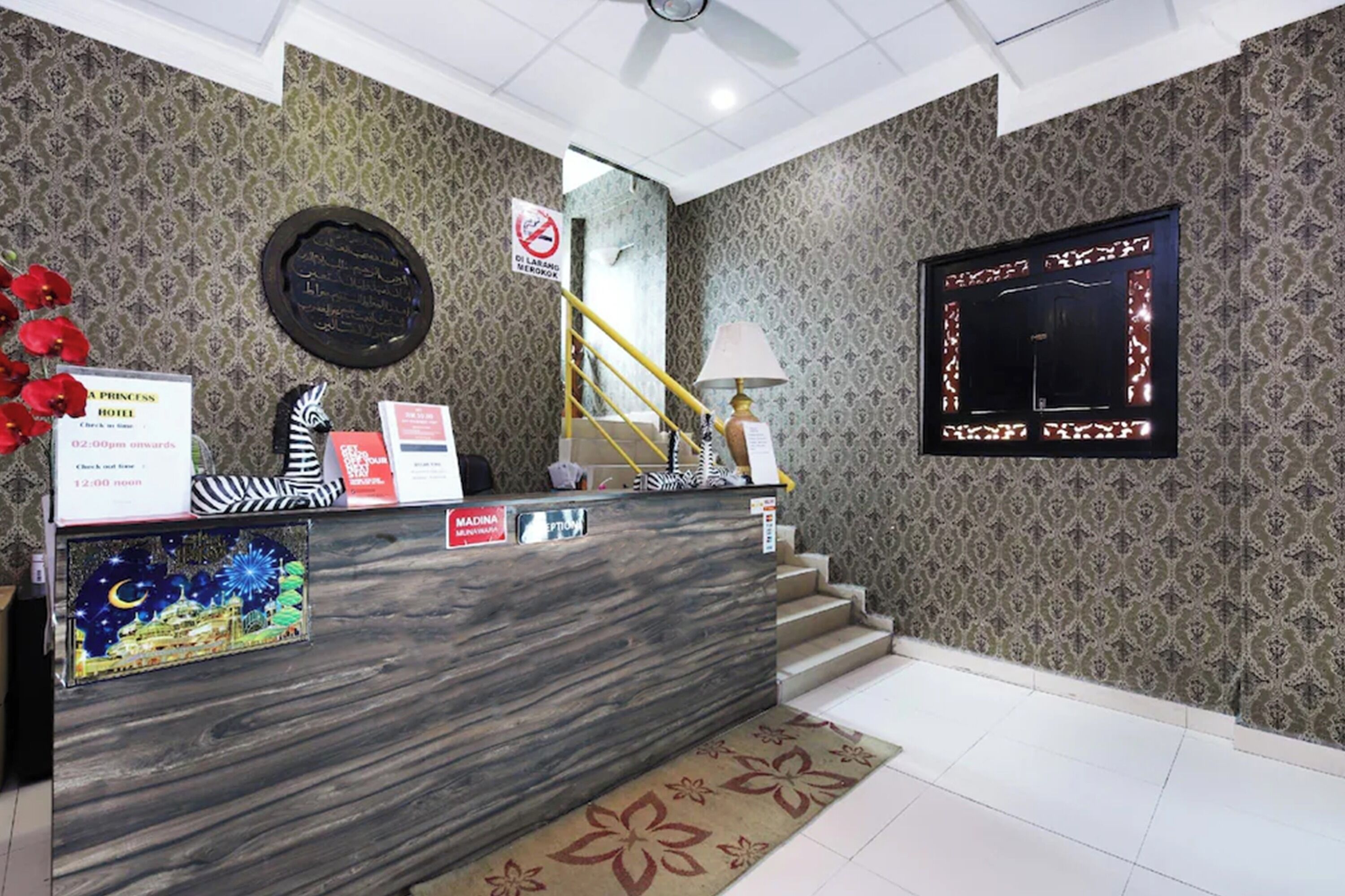 A hotel reception area with a marble counter, a staircase, and patterned wallpaper.