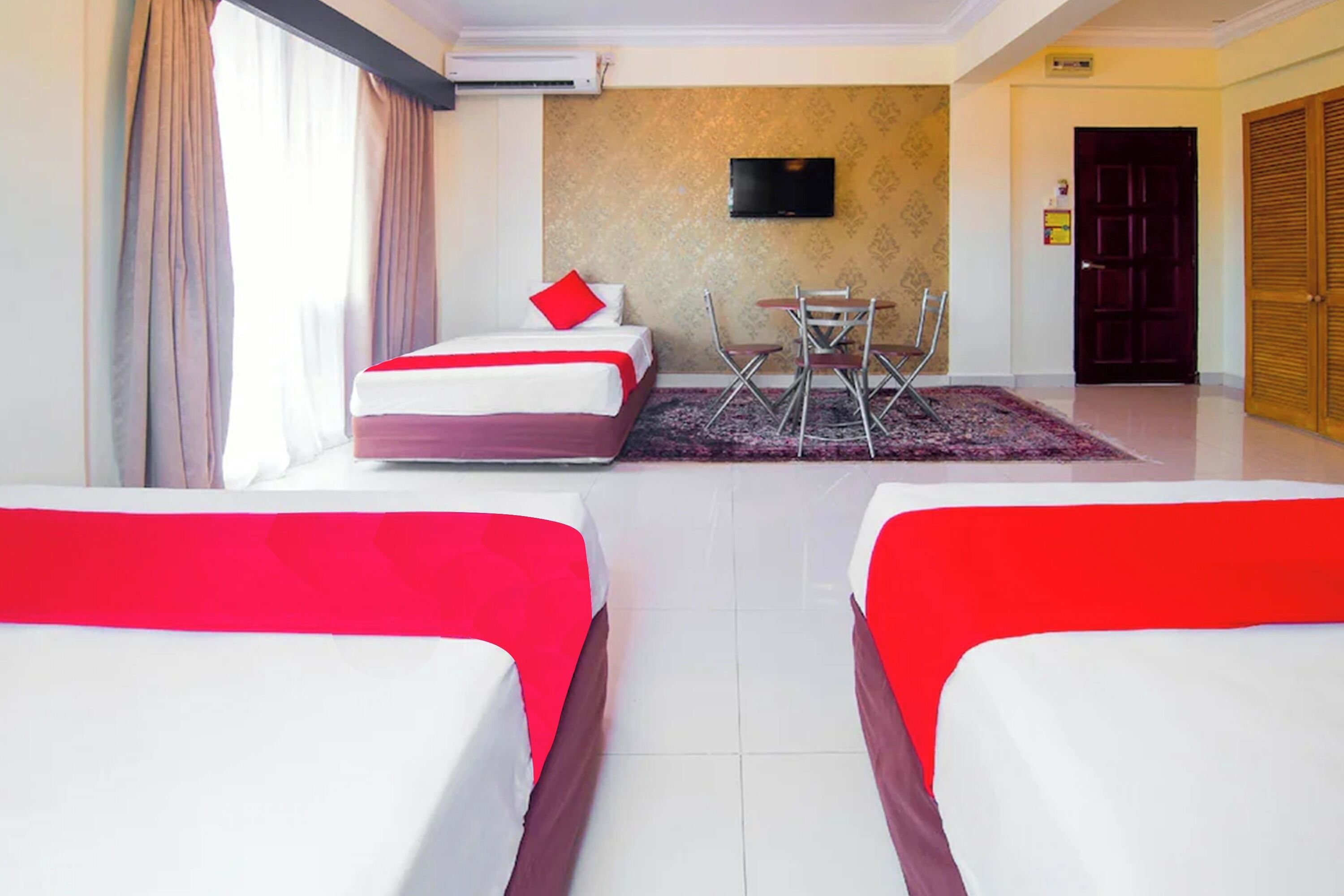 A hotel room with two beds, a TV, a desk with chairs, and a door.