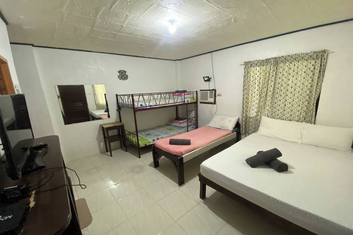 A bedroom with a bunk bed, a desk with a computer, a chair, a bed with pillows, and a curtain.
