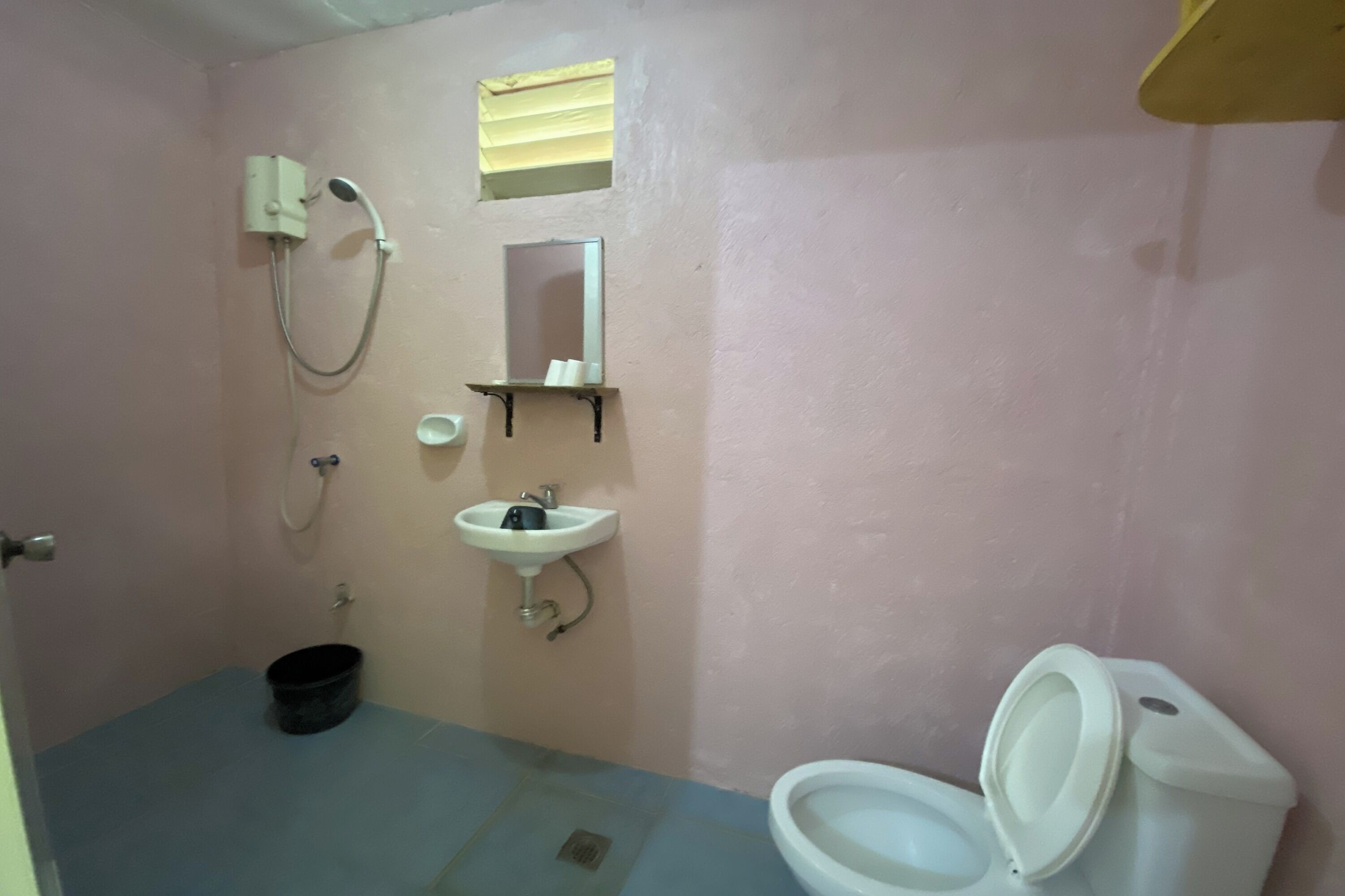 A bathroom with a toilet, sink, shower, and a small window.