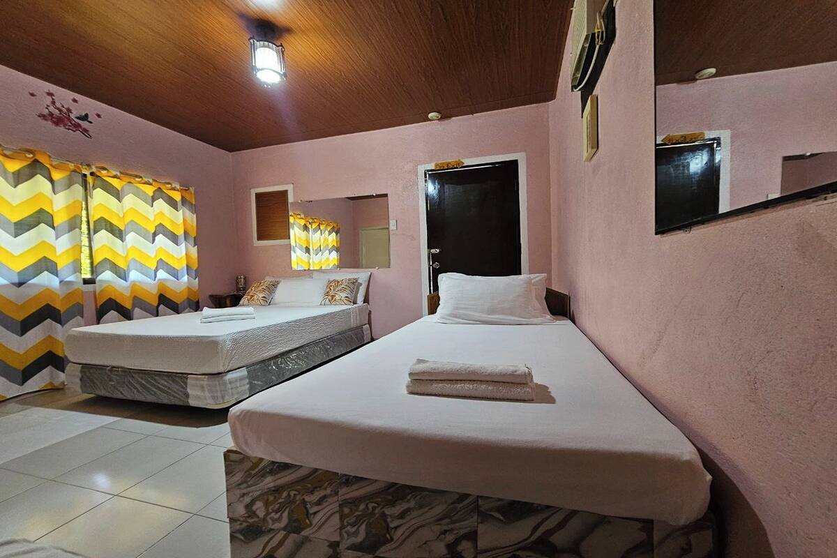 A room with two beds, a wooden ceiling, a mirror, and a window with curtains.