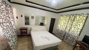 A hotel room with a bed, a small table, a TV, and curtains with a leaf pattern. - D & A Seaside Cottages (Catarman)